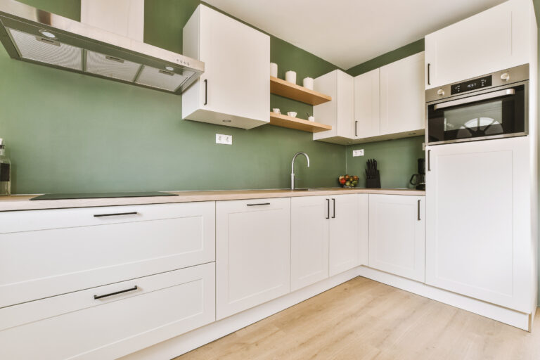 Fragment of interior of light narrow home kitchen with minimalist style white furniture with sink and stove